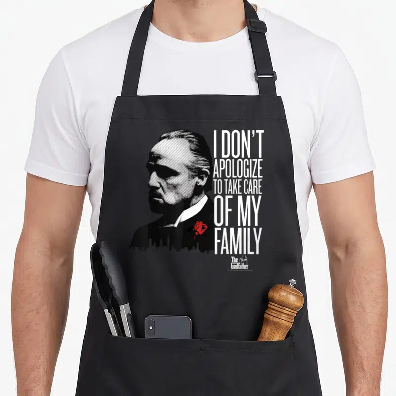 Apologize family aprons - Distressed man portrait with skyline torso, red rose, and stacked white text — shown on a black cotton canvas apron against a white background
