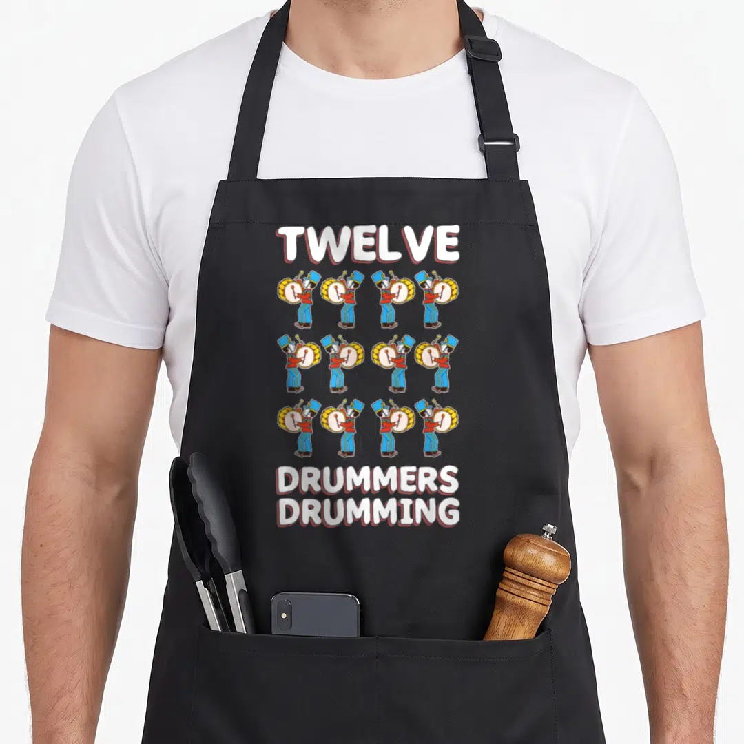 Drummer christmas apron - Twelve cartoon drummers in red blue yellow uniforms with TWELVE DRUMMERS DRUMMING text — shown on a black cotton canvas apron against a white background