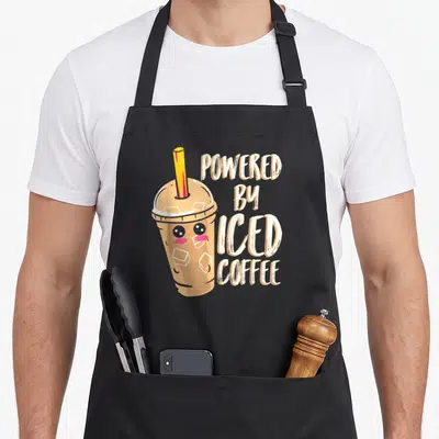 Iced anime apron - Cartoon iced coffee cup with yellow straw next to stacked POWERED BY ICED COFFEE text in light brown — shown on a black cotton canvas apron against a white background