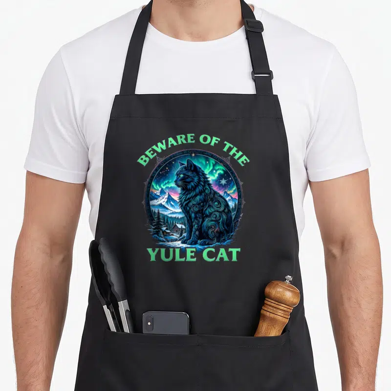 Beware christmas cat apron - Blue cat in snowy landscape with Beware of the Yule Cat text — shown on a black cotton canvas apron against a white background