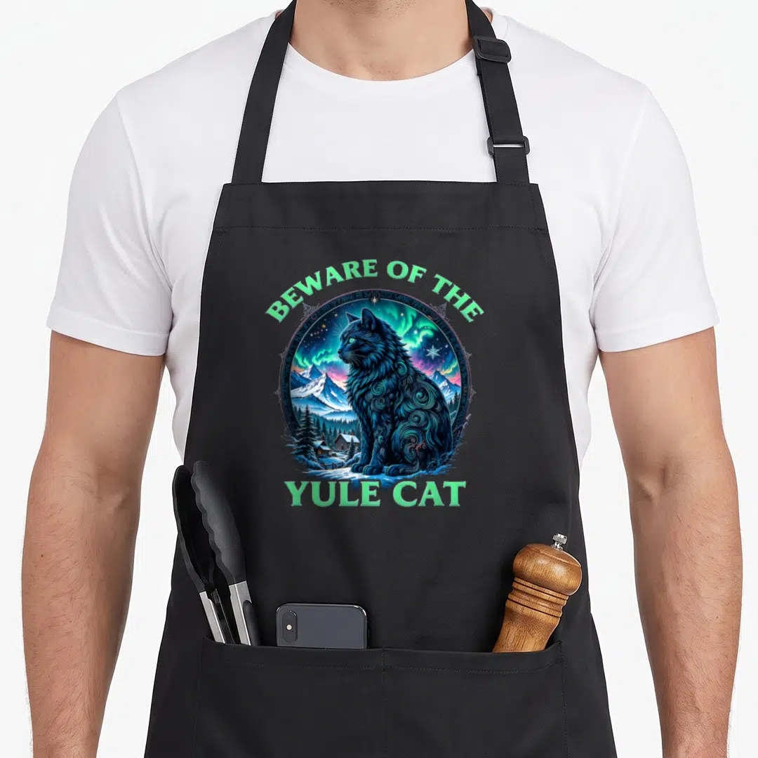 Beware christmas cat apron - Blue cat in snowy landscape with Beware of the Yule Cat text — shown on a black cotton canvas apron against a white background