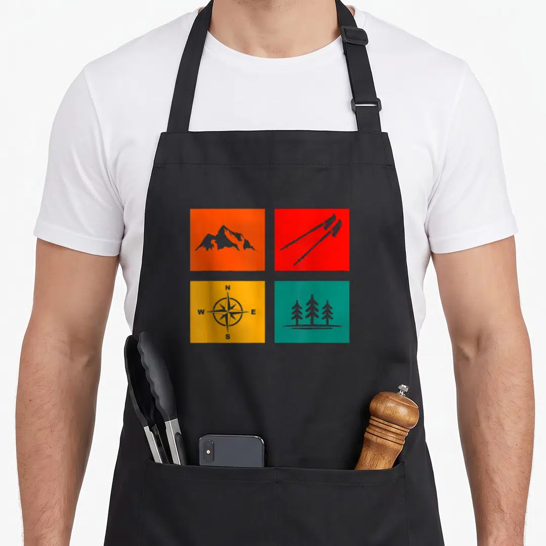 Outdoor backpacking hiking camping apron - Four colored squares with grey mountain, skis, compass, and tree silhouettes — shown on a black cotton canvas apron against a white background