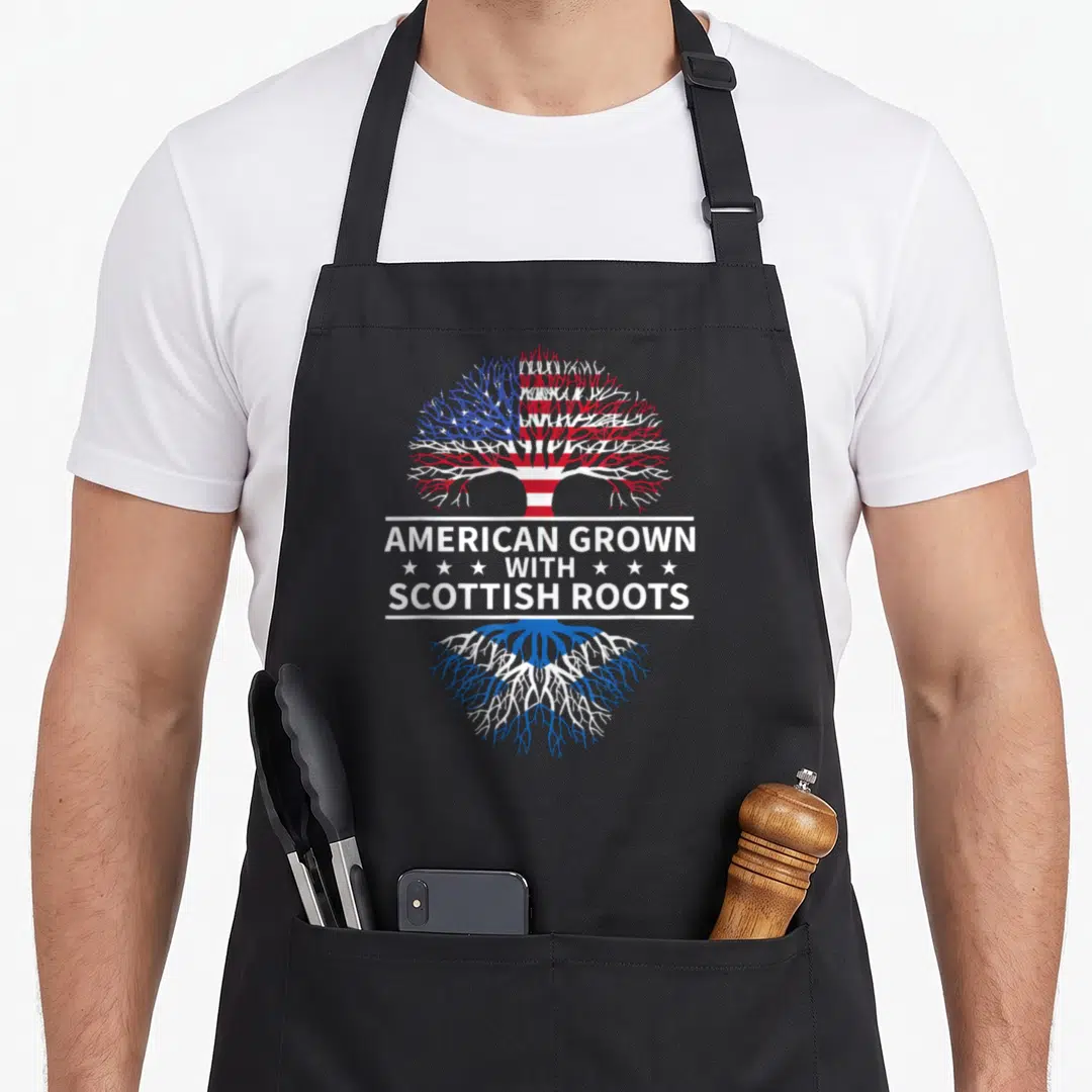 Grown scotland apron - Tree with USA flag canopy and Scottish flag roots separated by text banner with six stars — shown on a black cotton canvas apron against a white background
