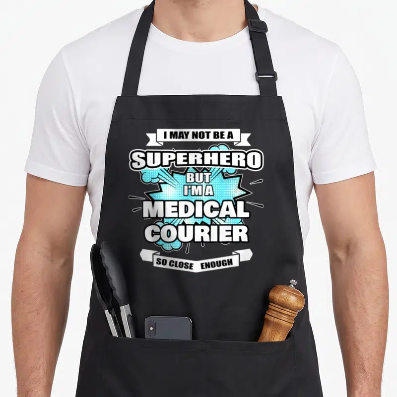Medical superhero apron - Stacked text on white ribbons over light blue halftone burst reading I may not be a superhero — shown on a black cotton canvas apron against a white background