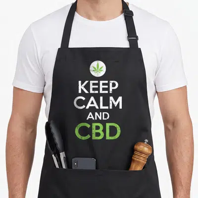 Cbd cannabidiol hemp apron - Green cannabis leaf in white circle above stacked distressed text reading KEEP CALM AND CBD — shown on a black cotton canvas apron against a white background