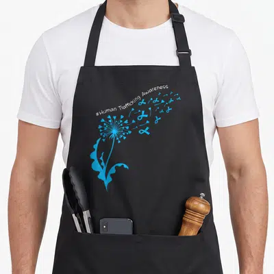Dandelion human trafficking awareness apron - Blue dandelion seeds turn into hearts and ribbons under white arched text — shown on a black cotton canvas apron against a white background