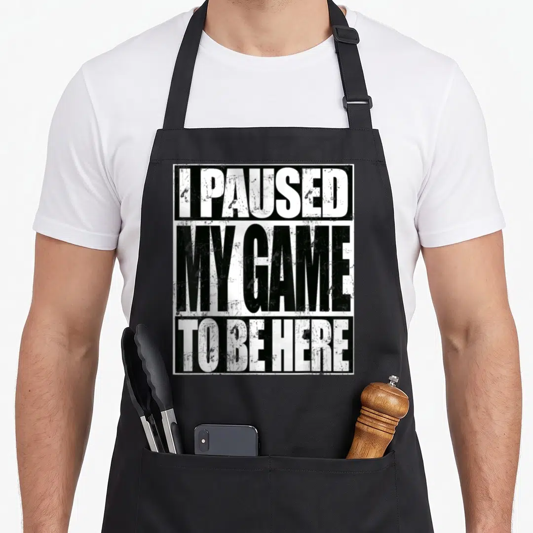 Paused sarcastic apron - Stacked white and black text reading I Paused My Game To Be Here with distressed finish — shown on a black cotton canvas apron against a white background