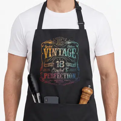 Limited born day apron - Retro vintage 2007 18 years matured text design in orange blue red and white swirls — shown on a black cotton canvas apron against a white background
