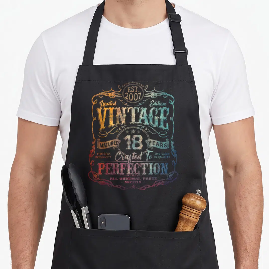 Limited born day apron - Retro vintage 2007 18 years matured text design in orange blue red and white swirls — shown on a black cotton canvas apron against a white background
