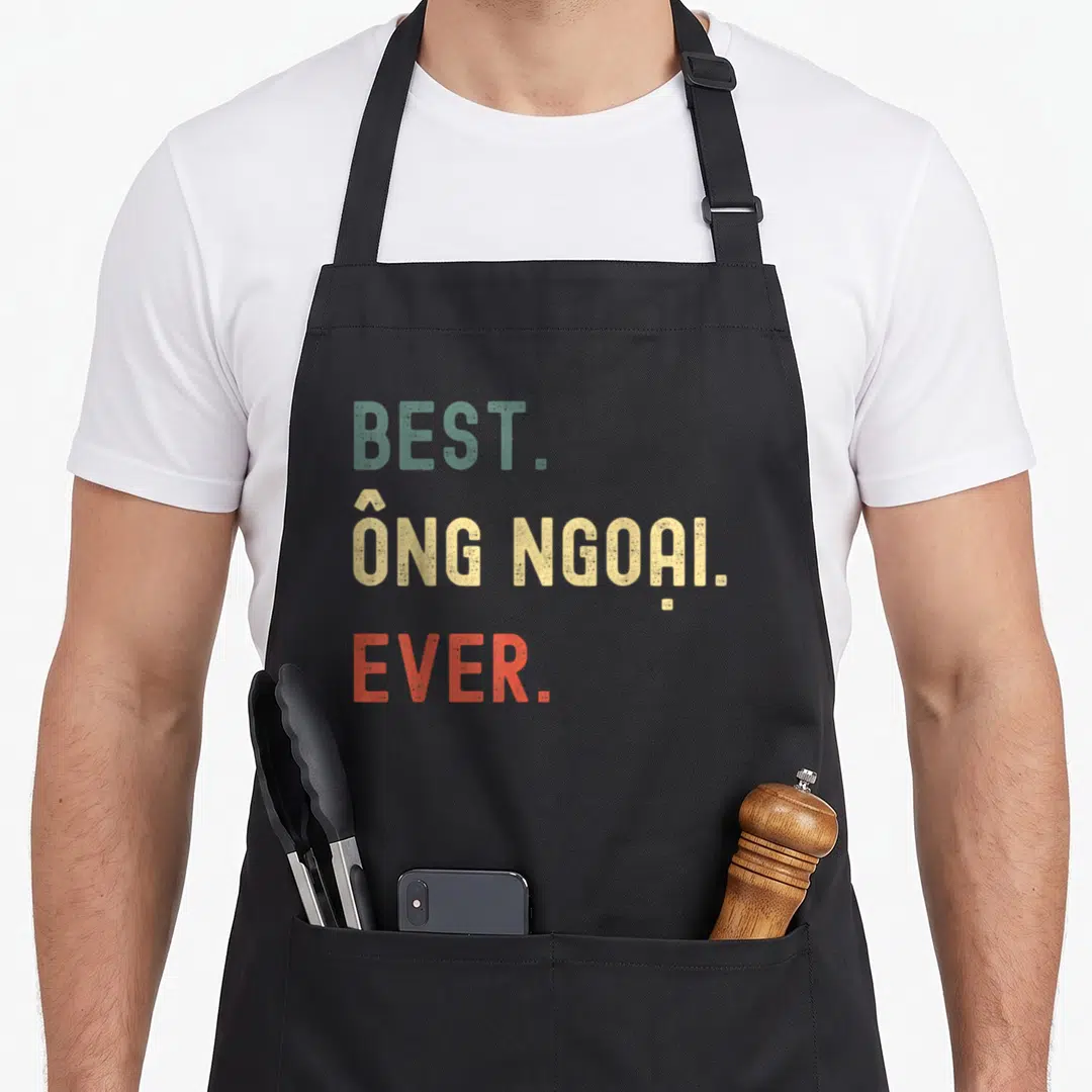 Vietnamese grandpa apron - Stacked text reading BEST ONG NGOAI EVER in green yellow and red distressed font — shown on a black cotton canvas apron against a white background