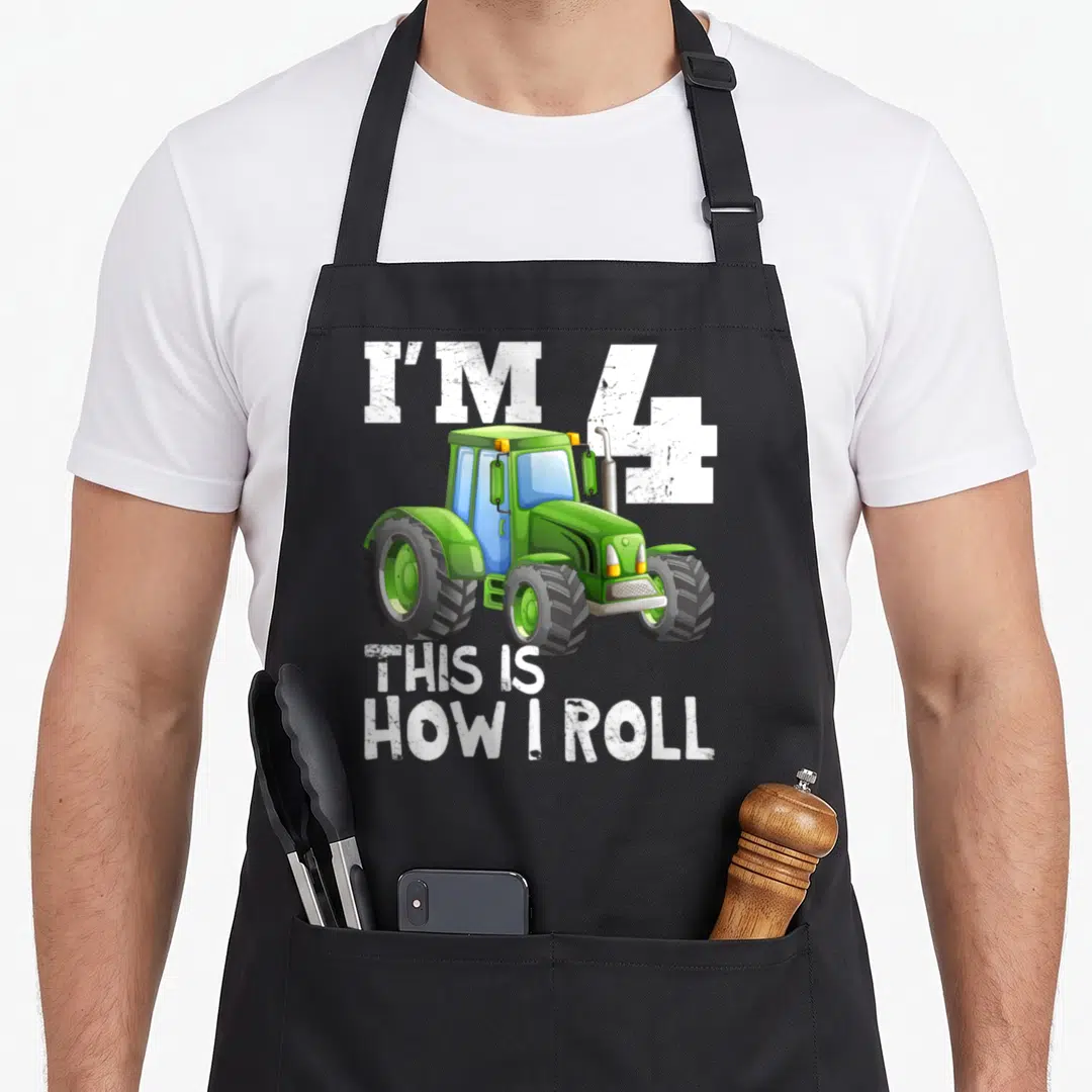 4th farm apron - Green cartoon tractor with white text reading I'M 4 THIS IS HOW I ROLL — shown on a black cotton canvas apron against a white background