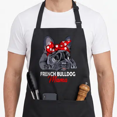 Mama french bulldog apron - Grey cartoon French Bulldog head with red polka dot bow and stacked white and red text — shown on a black cotton canvas apron against a white background