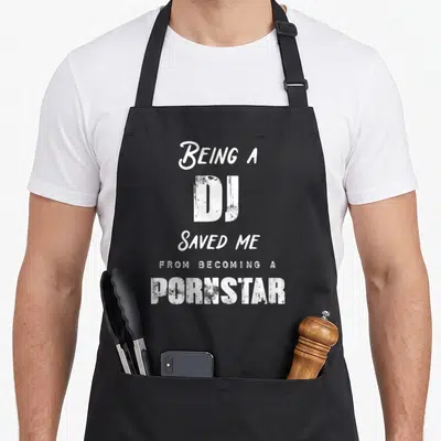 Saved nurse apron - White stacked text reading Being a DJ Saved Me from Becoming a Pornstar — shown on a black cotton canvas apron against a white background