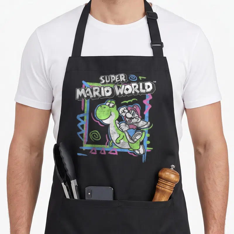 90s holiday apron - Super Mario World text, Yoshi, Mario, and abstract swirls in green, blue, pink, and white — shown on a black cotton canvas apron against a white background