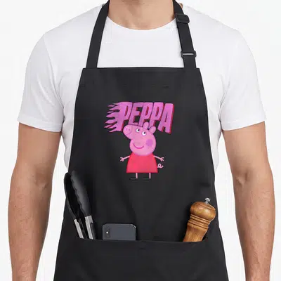 Funny flame apron - Peppa Pig character in red dress below pink text with speed lines on black fabric — shown on a black cotton canvas apron against a white background