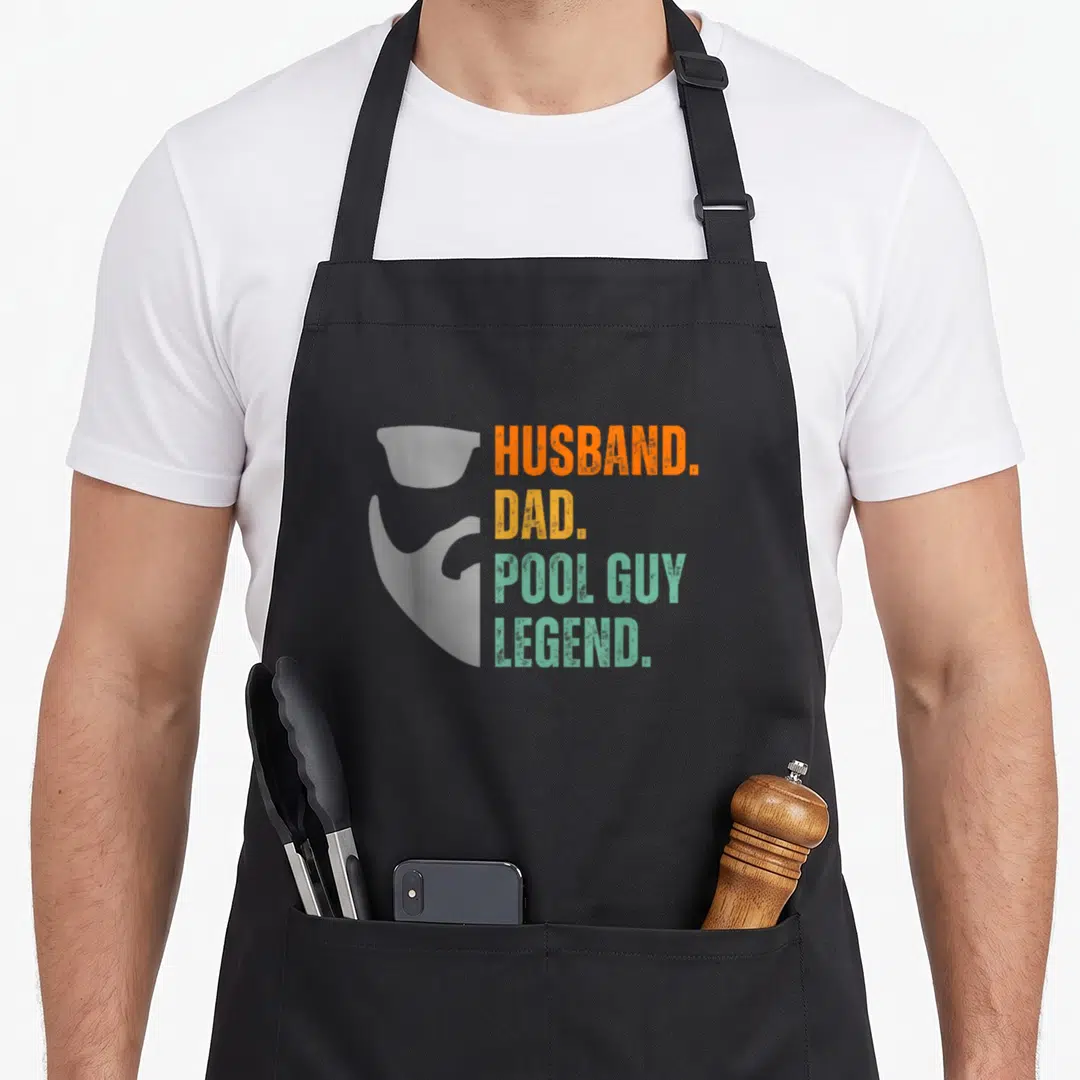 Funny pool husband apron - Grey bearded man silhouette next to stacked HUSBAND DAD POOL GUY LEGEND text in orange — shown on a black cotton canvas apron against a white background