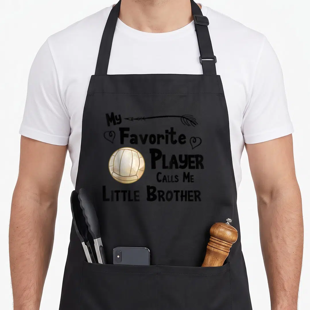 Brother game aprons - Stacked text My Favorite Player Calls Me Little Brother with arrow, two hearts, and gold-trimmed — shown on a black cotton canvas apron against a white background