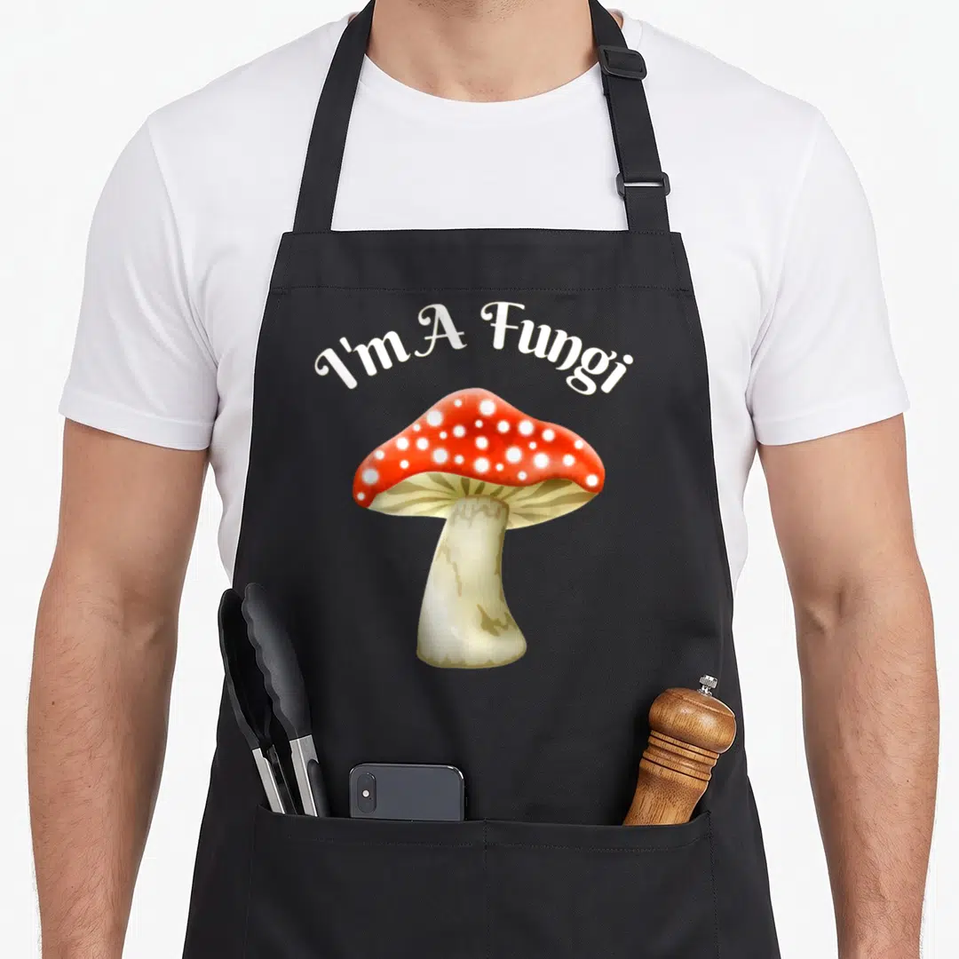 Humorous mushroom apron - I'm A Fungi text over red spotted mushroom illustration — shown on a black cotton canvas apron against a white background