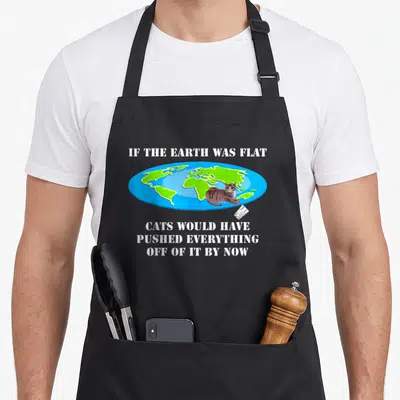 Earth cat apron - Cartoon cat on flat earth map with falling glass and sarcastic white stencil text — shown on a black cotton canvas apron against a white background