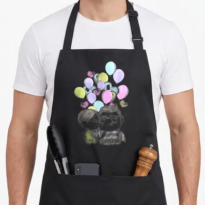 Ellie valentine apron - Cartoon couple kissing under heart-shaped balloons in grey, pink, blue, yellow, and purple — shown on a black cotton canvas apron against a white background