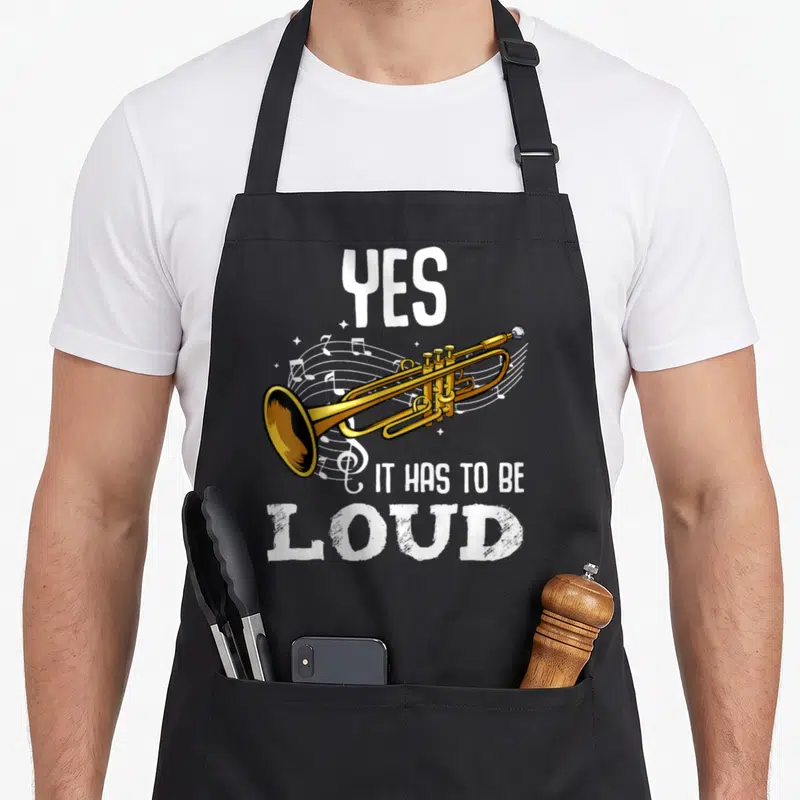 Das tablet apron - Gold trumpet with white musical notes and text YES IT HAS TO BE LOUD — shown on a black cotton canvas apron against a white background