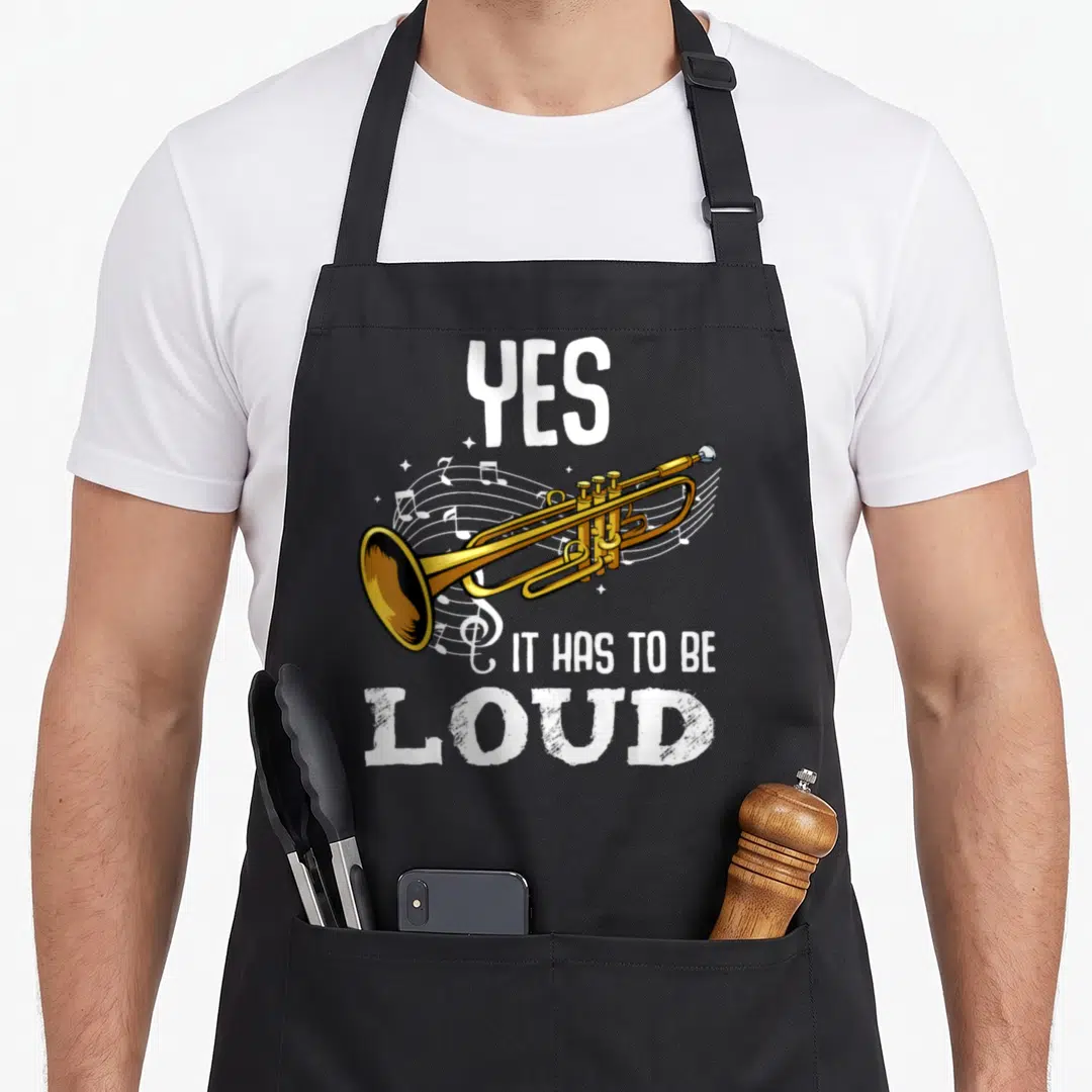 Das tablet apron - Gold trumpet with white musical notes and text YES IT HAS TO BE LOUD — shown on a black cotton canvas apron against a white background