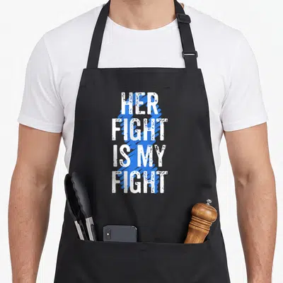Fight colon cancer awareness apron - White distressed text Her Fight Is My Fight over a blue ribbon shape — shown on a black cotton canvas apron against a white background