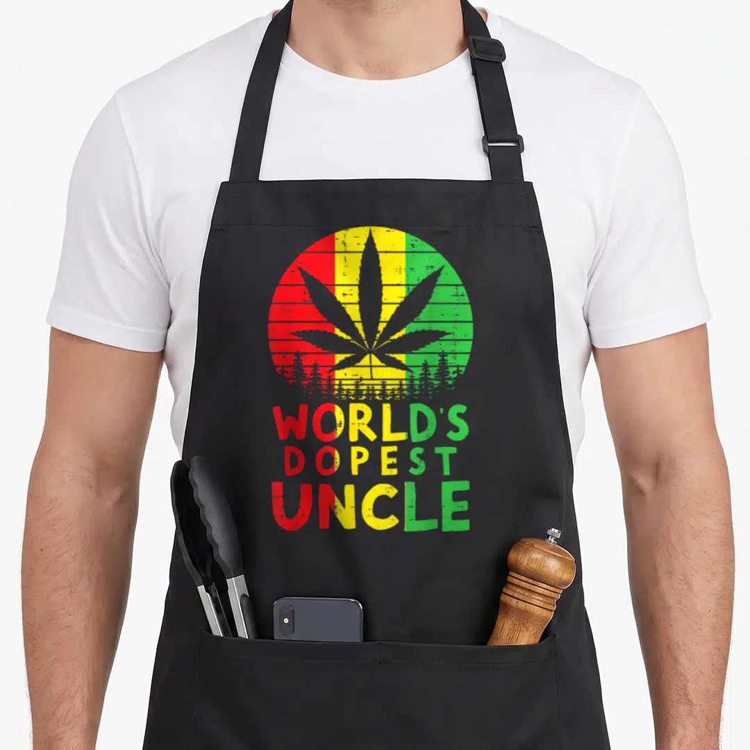 Dopest hemp lover apron - Grey cannabis leaf in red yellow green circle with forest base and stacked WORLD'S DOPEST — shown on a black cotton canvas apron against a white background