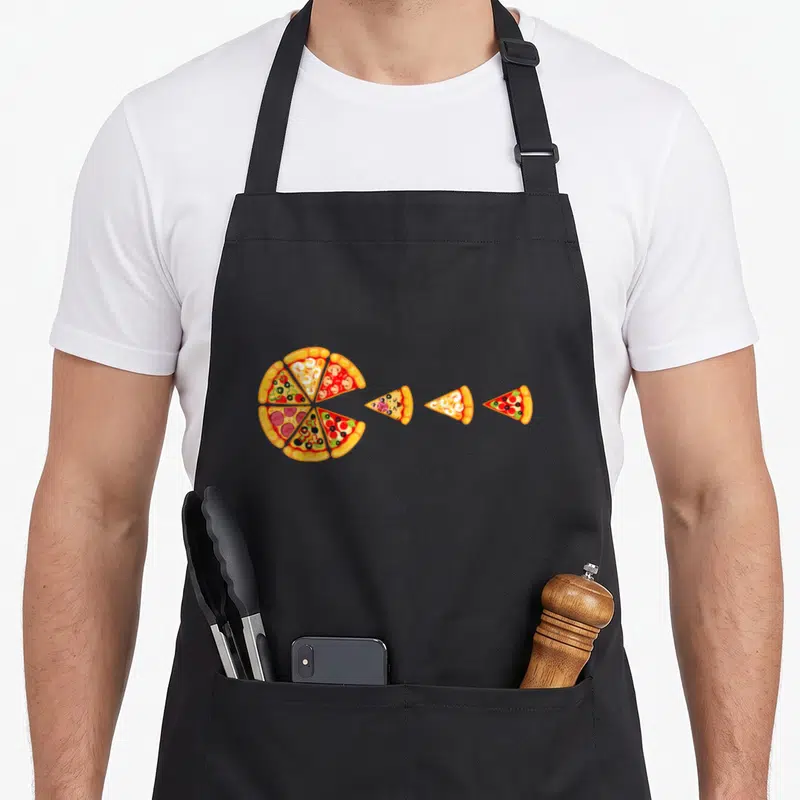 Pizza pie apron - Cartoon pizza with three slices in yellow, red, and green — shown on a black cotton canvas apron against a white background