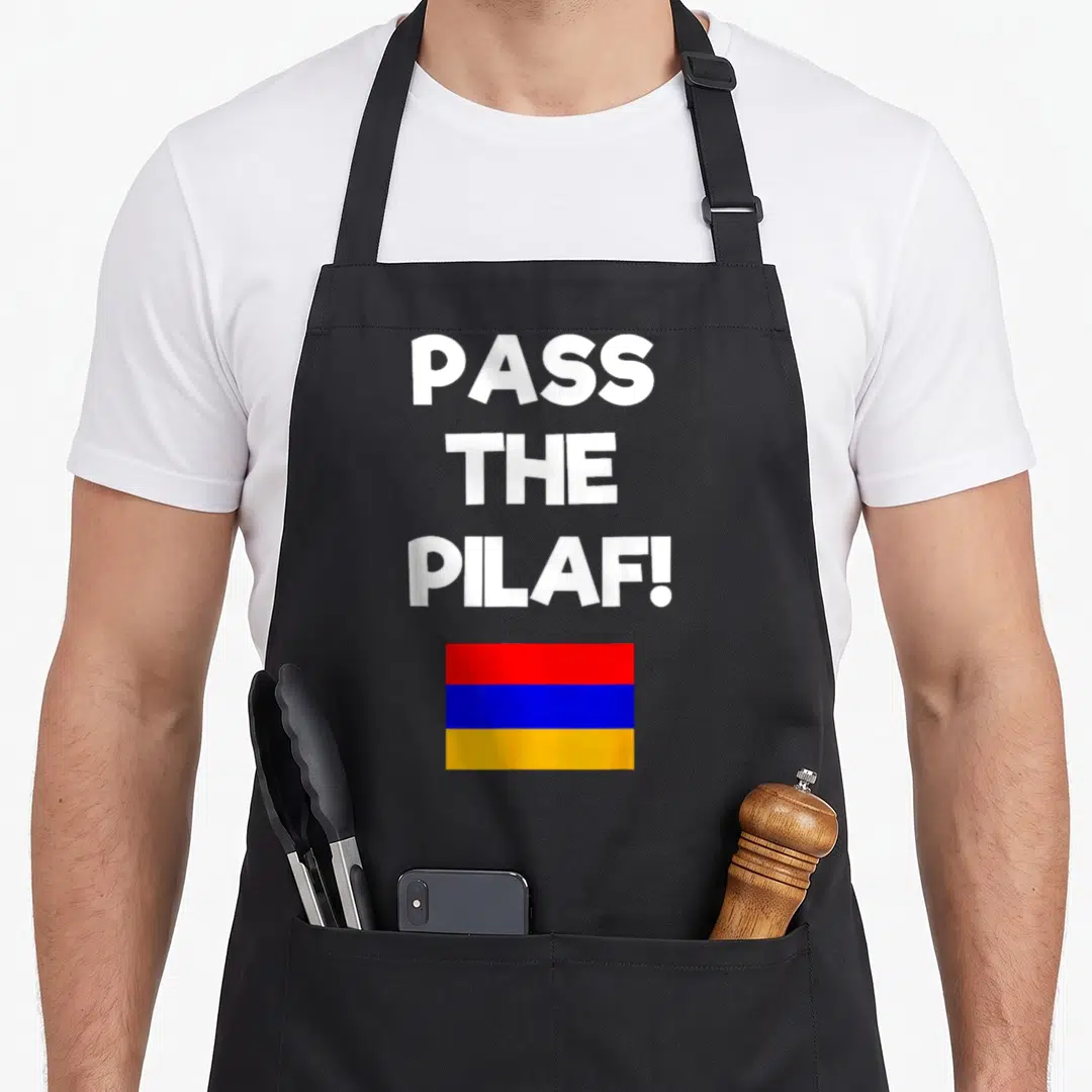Pass family aprons - White text PASS THE PILAF! above red blue and orange Armenian flag — shown on a black cotton canvas apron against a white background