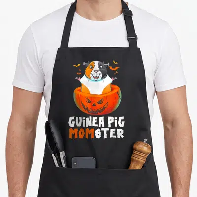 Guinea halloween apron - Cartoon guinea pig frankenstein in orange pumpkin with bats and stacked text — shown on a black cotton canvas apron against a white background