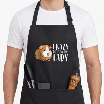 Funny guinea pet apron - Cartoon guinea pig in white brown pink next to three lines of text — shown on a black cotton canvas apron against a white background
