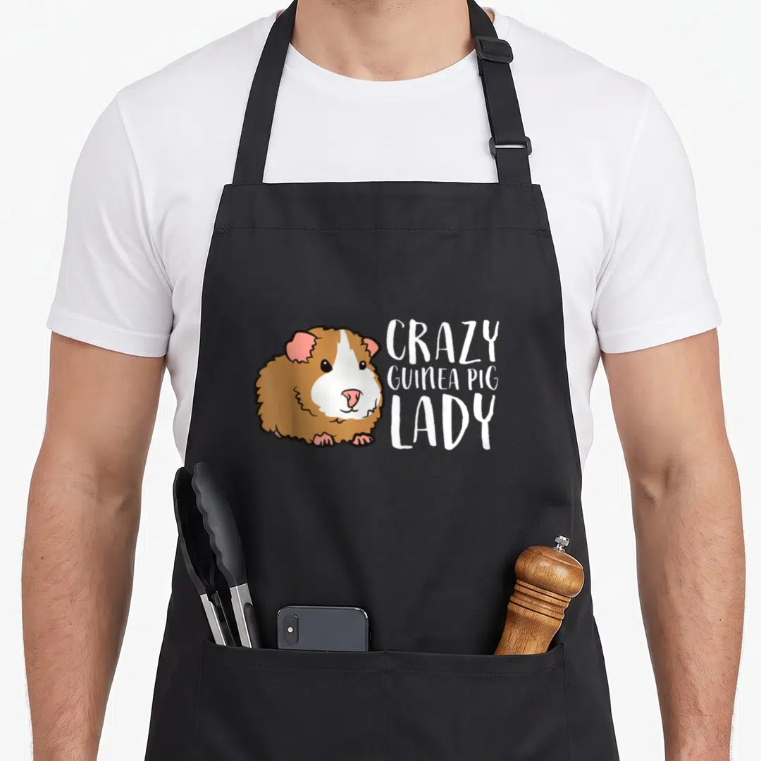 Funny guinea pet apron - Cartoon guinea pig in white brown pink next to three lines of text — shown on a black cotton canvas apron against a white background