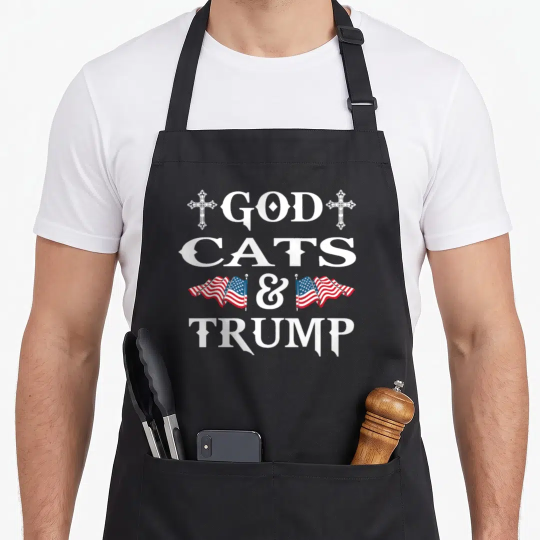 Election cat apron - Stacked white text GOD CATS & TRUMP with crosses and flags in red white blue — shown on a black cotton canvas apron against a white background