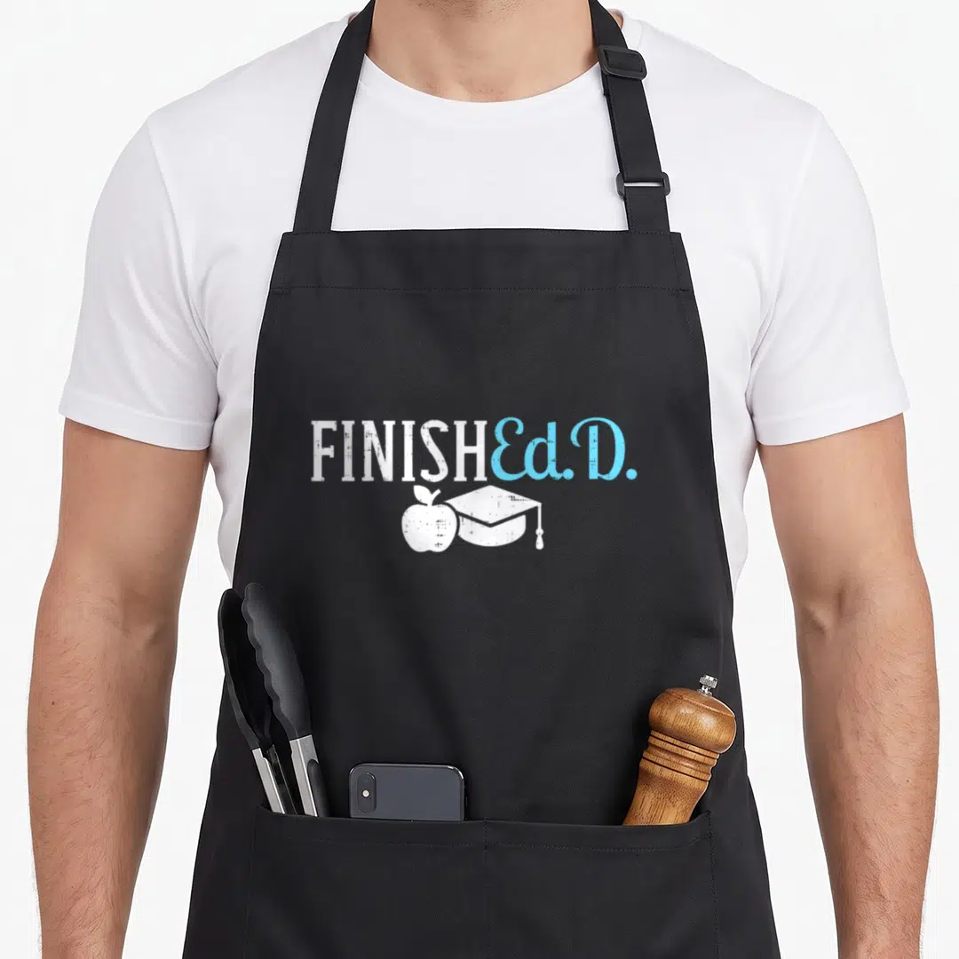 Finishedd doctor apron - FINISHED Ed.D. text in white and blue above a white apple and mortarboard icon — shown on a black cotton canvas apron against a white background