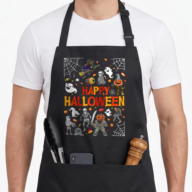 Funny scary halloween apron - Cartoon monsters, candy, webs, and HAPPY HALLOWEEN text in orange and red — shown on a black cotton canvas apron against a white background
