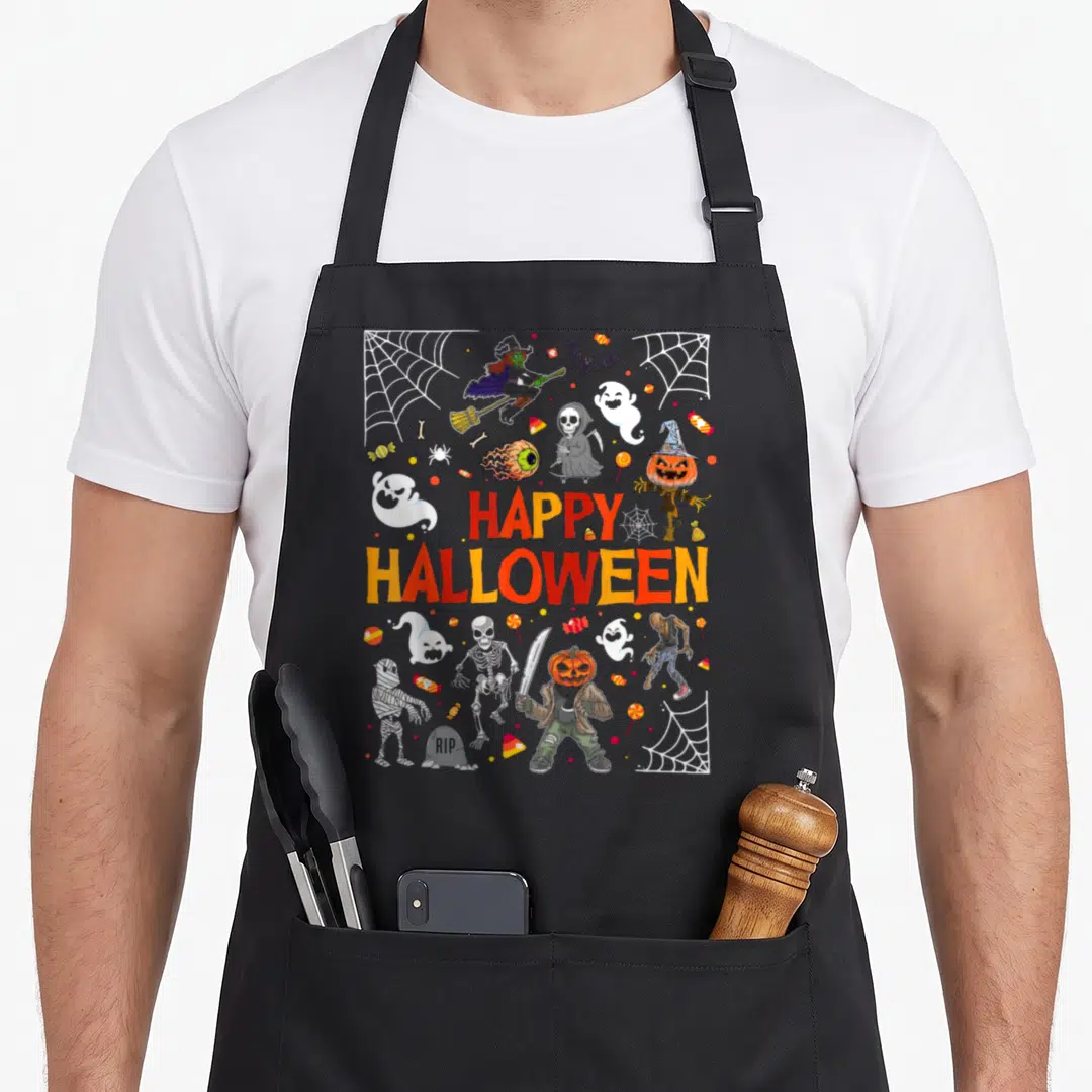 Funny scary halloween apron - Cartoon monsters, candy, webs, and HAPPY HALLOWEEN text in orange and red — shown on a black cotton canvas apron against a white background