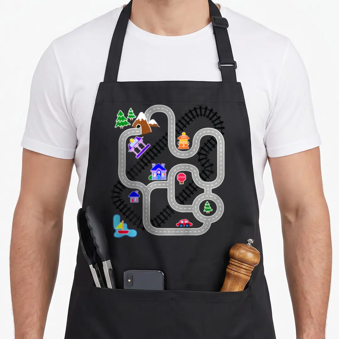 Father car apron - Winding white road, black railroad tracks, gas station, stop sign, red car, blue house, green trees — shown on a black cotton canvas apron against a white background