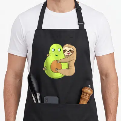 Lazy avocado apron - Cartoon sloth hugging large green avocado with brown pit and claws visible — shown on a black cotton canvas apron against a white background