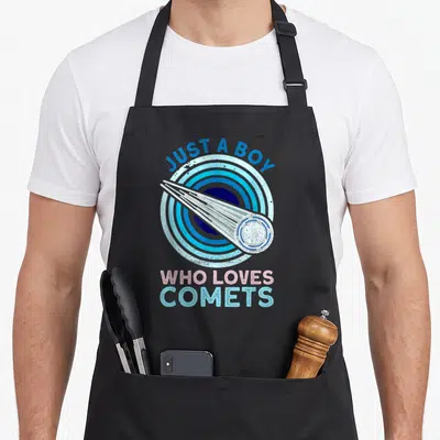 Astronomical comet apron - JUST A BOY WHO LOVES COMETS text over blue concentric circles and white comet graphic — shown on a black cotton canvas apron against a white background