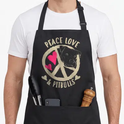 Pitbull taurus girl apron - Beige peace sign with pink hearts and pitbull head surrounded by arched text — shown on a black cotton canvas apron against a white background