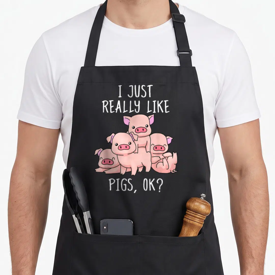 Swine pig lover apron - Four pink cartoon pigs stacked under text I JUST REALLY LIKE PIGS OK — shown on a black cotton canvas apron against a white background