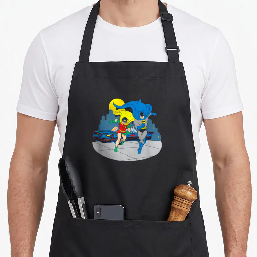 Midnight animal apron - Retro cartoon Batman and Robin running past a blue Batmobile and city skyline under a yellow sun — shown on a black cotton canvas apron against a white background