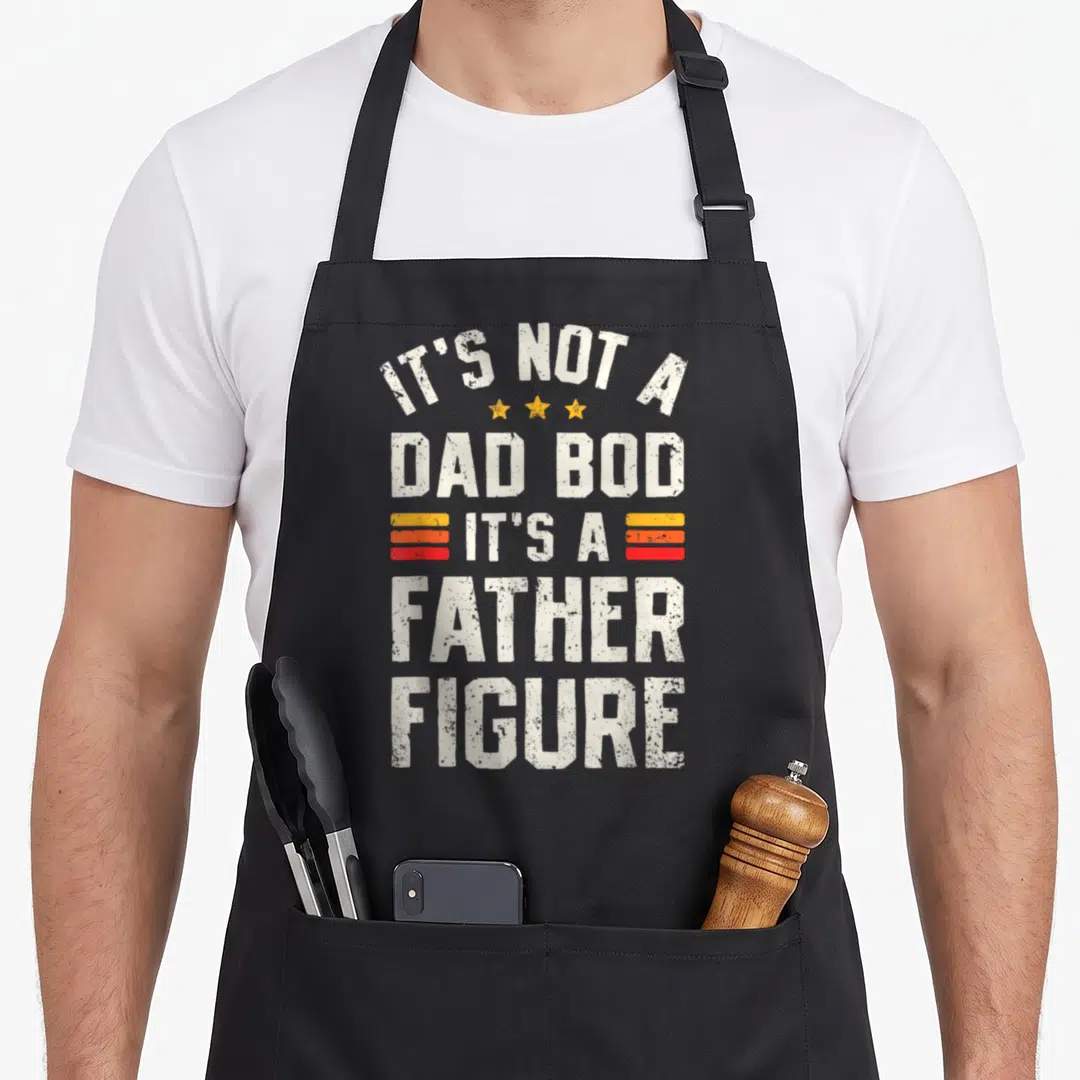Cute bod father day apron - Distressed white text reading IT'S NOT A DAD BOD IT'S A FATHER FIGURE with three yellow — shown on a black cotton canvas apron against a white background