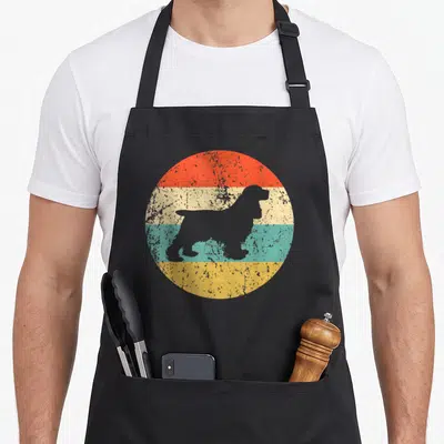 Funny dog cocker spaniel apron - Grey Cocker Spaniel silhouette on distressed orange cream teal and yellow stripes — shown on a black cotton canvas apron against a white background