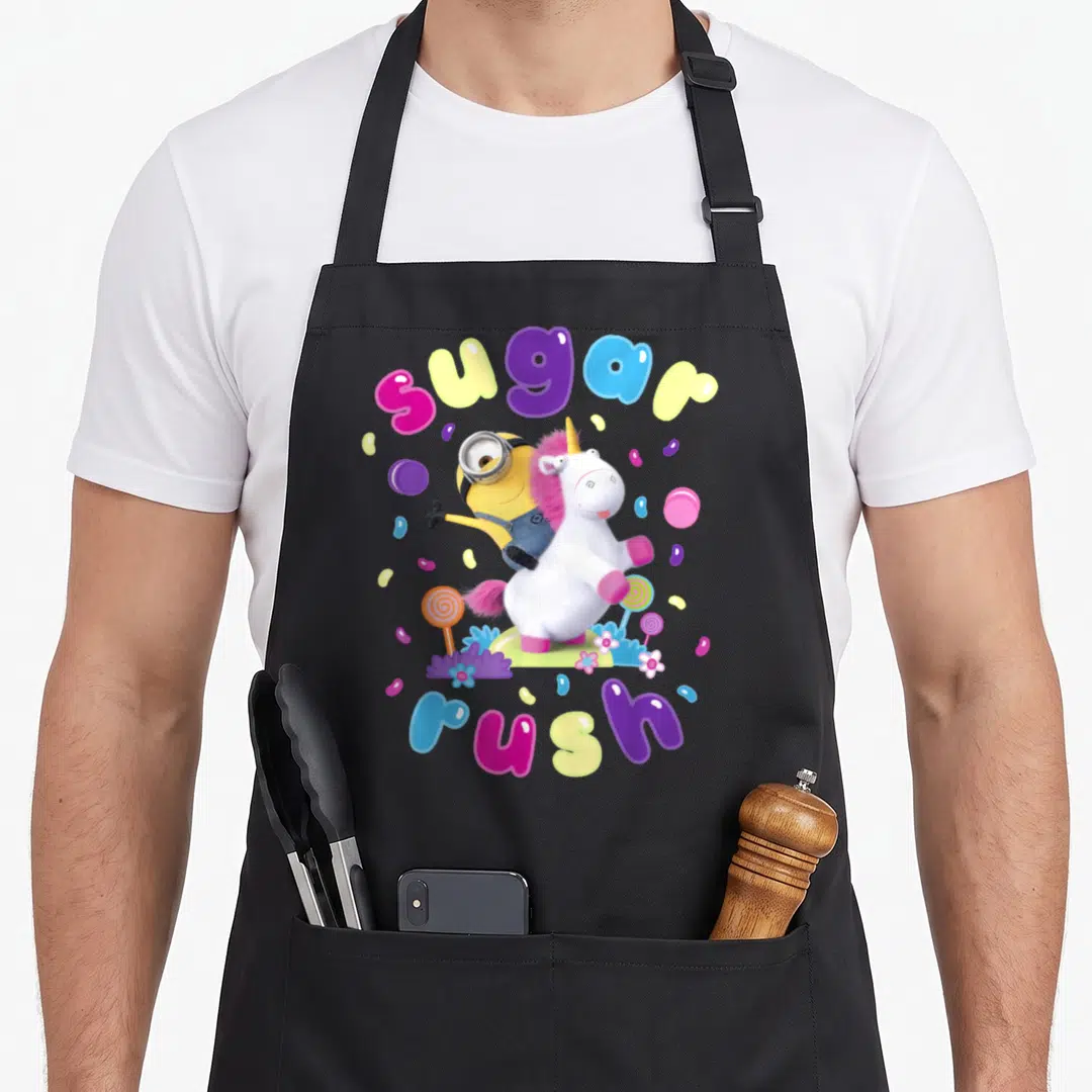 Despicable cotton candy apron - Yellow Minion riding a white unicorn with sugar rush text and scattered candy graphics — shown on a black cotton canvas apron against a white background