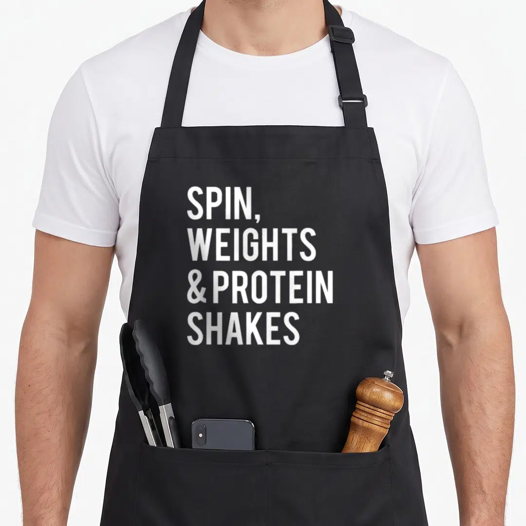 Weight spinning apron - White stacked text reading SPIN WEIGHTS & PROTEIN SHAKES on grey background — shown on a black cotton canvas apron against a white background