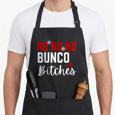 Bunco christmas apron - Red and white stacked text reading Ho Ho Ho Bunco Bitches with three snowflakes — shown on a black cotton canvas apron against a white background