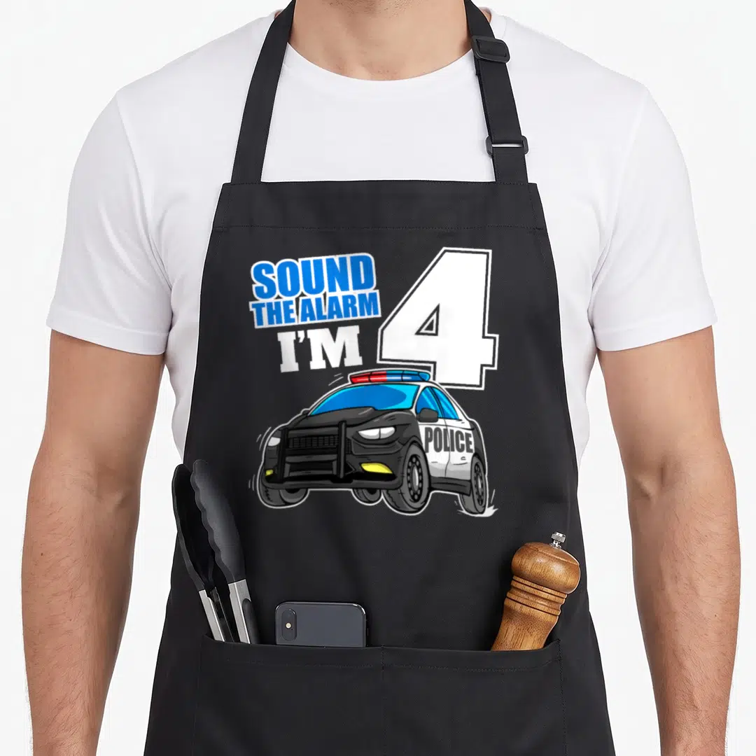 Police car apron - SOUND THE ALARM I'M 4 text with cartoon police car in blue and white — shown on a black cotton canvas apron against a white background