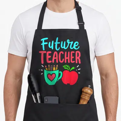Education teacher apron - Future TEACHER text above green pencil cup and red apple cartoon — shown on a black cotton canvas apron against a white background